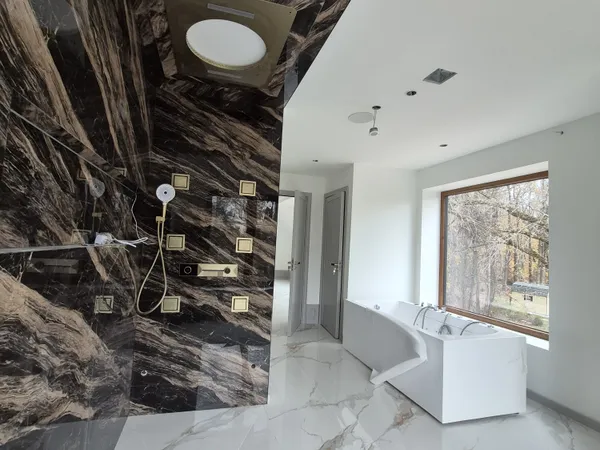 Luxury master bathroom — bookmatched marble shower wall, brass fixtures, freestanding smart-control tub