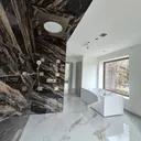 Luxury master bathroom — bookmatched marble shower wall, brass fixtures, freestanding smart-control tub