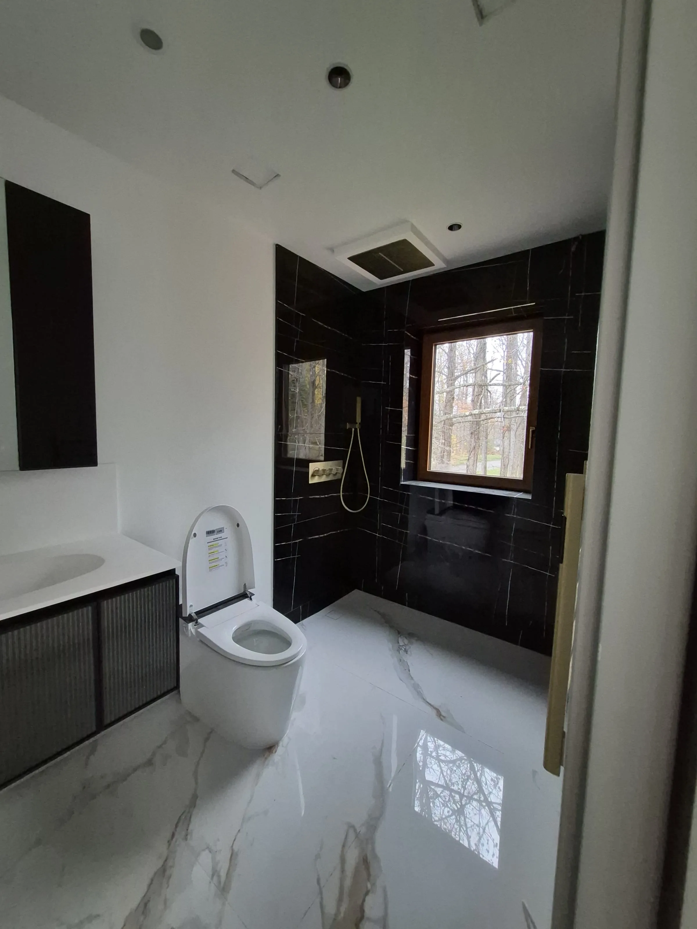 Bookmatched marble shower wall behind a sensor-controlled smart toilet — mirrored veining across two adjacent slabs