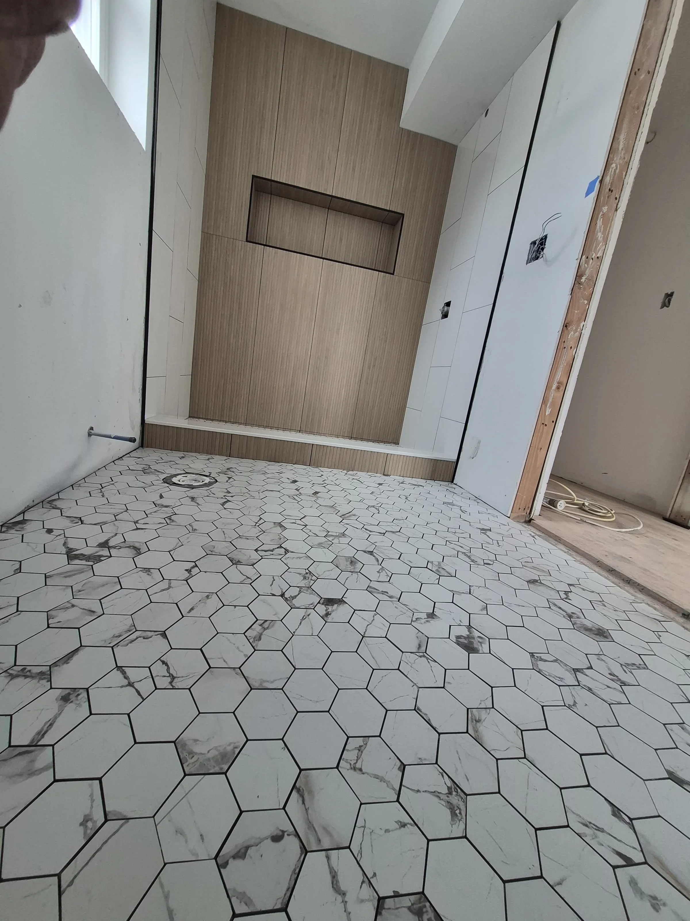 Bookmatched calacatta marble shower wall in a Manhattan bathroom — two slabs from the same block opened across a 6-foot wall, mitred outside corners, slab niche, slab curb
